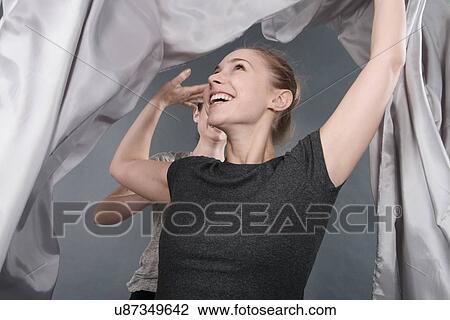Stock Image - Young women holding cloth over head, grey background. Fotosearch