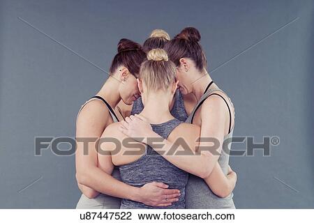 Stock Image - Young women in a huddle, grey background. Fotosearch