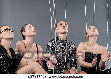 Stock Photo - Young women looking at hanging strings, grey background. Fotosearch
