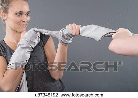 Stock Image - Young women playing tug of war, grey background. Fotosearch