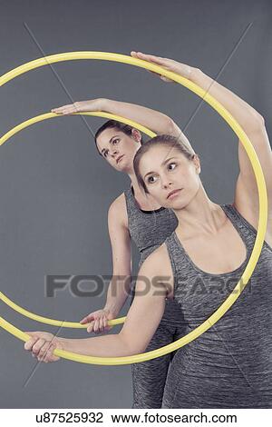 Stock Image - Young women practising with hula hoop, grey background. Fotosearch