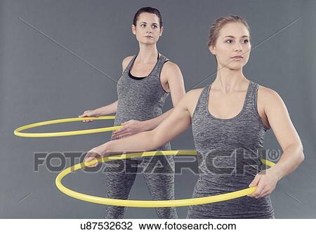 Stock Image - Young women practising with hula hoop, grey background. Fotosearch
