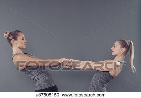 Stock Image - Young women stretching, holding hands, grey background. Fotosearch
