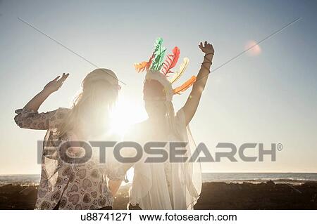 Young women wearing feather headdress arms raised dancing in sunlight View Large Photo Image Stock Image - Young women wearing feather headdress arms raised dancing in sunlight. Fotosearch