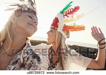 Stock Image - Young women wearing feather headdresses looking away smiling. Fotosearch