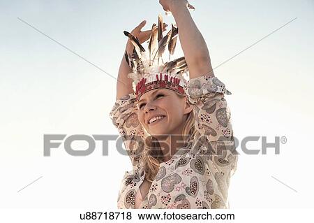 Young women wearing feather headdresses dancing, arms raised looking away smiling View Large Photo Image Stock Photo - Young women wearing feather headdresses dancing, arms raised looking away smiling. Fotosearch