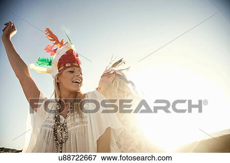 Stock Photo - Young women wearing feather headdresses dancing in sunlight smiling. Fotosearch