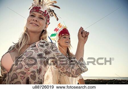 Stock Photo - Young women wearing feather headdresses dancing, looking at camera smiling. Fotosearch