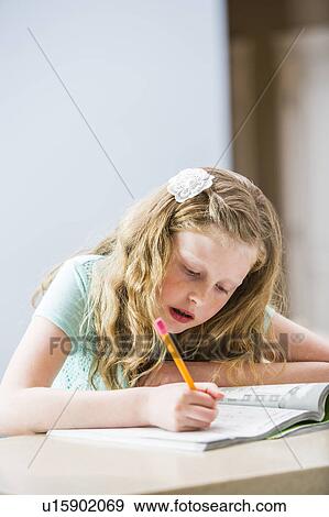 Stock Photo - Blonde girl (8-9) doing homework at table. Fotosearch
