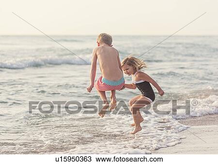 Boy (6-7) and girl (4-5) jumping in water on beach View Large Photo Image Stock Image - Boy (6-7) and girl (4-5) jumping in water on beach. Fotosearch