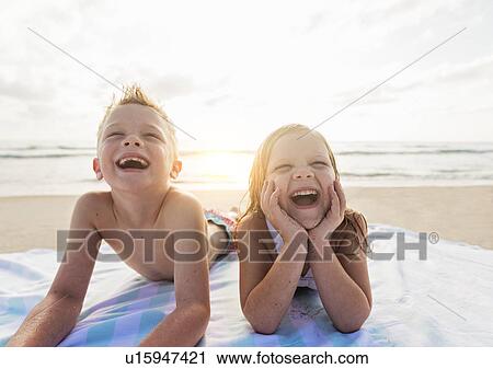 Stock Image - Boy (6-7) and girl (4-5) lying on beach laughing. Fotosearch