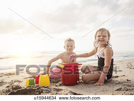 Picture - Boy (6-7) and girl (4-5) playing with sand on beach. Fotosearch