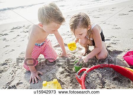 Boy (6-7) and girl (4-5) playing with sand on beach View Large Photo Image Stock Image - Boy (6-7) and girl (4-5) playing with sand on beach. Fotosearch
