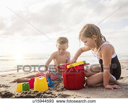 Stock Image - Boy (6-7) and girl (4-5) playing with sand on beach. Fotosearch