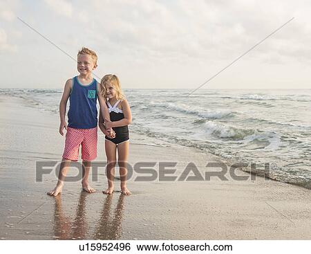 Boy (6-7) and girl (4-5) standing on beach by water holding hands View Large Photo Image Stock Photograph - Boy (6-7) and girl (4-5) standing on beach by water holding hands. Fotosearch