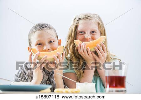 Stock Photo - Children (6-7, 8-9) eating cantaloupe for breakfast. Fotosearch