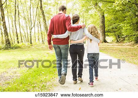 Stock Photo - Daughter (8-9) with parents walking in park, rear view. Fotosearch