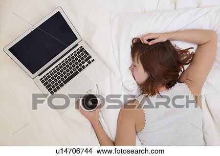 Exhausted woman in bed with laptop View Large Photo Image Picture - Exhausted woman in bed with laptop. Fotosearch