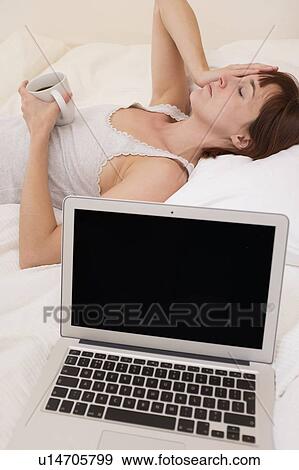 Exhausted woman in bed with laptop View Large Photo Image Stock Photo - Exhausted woman in bed with laptop. Fotosearch