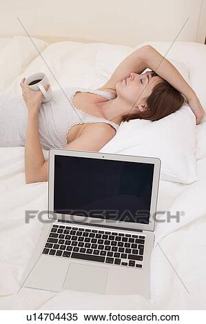 Stock Photography - Exhausted woman in bed with laptop. Fotosearch