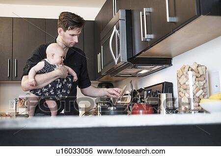 Father holding baby daughter (2-5 months) while stirring food View Large Photo Image Stock Photograph - Father holding baby daughter (2-5 months) while stirring food. Fotosearch