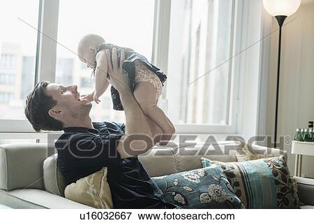 Father sitting on sofa and playing with baby daughter (2-5 months) View Large Photo Image Stock Photo - Father sitting on sofa and playing with baby daughter (2-5 months). Fotosearch