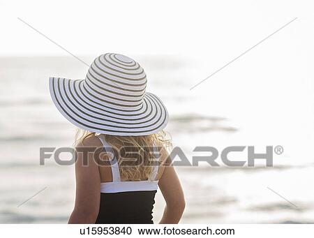 Stock Image - Girl (4-5) in striped sunhat by sea. Fotosearch