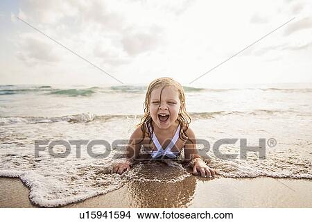 Picture - Girl (4-5) lying down in water on beach. Fotosearch