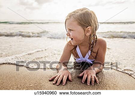 Stock Image - Girl (4-5) lying down in water on beach. Fotosearch
