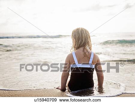 Girl (4-5) lying down in water on beach View Large Photo Image Stock Photo - Girl (4-5) lying down in water on beach. Fotosearch