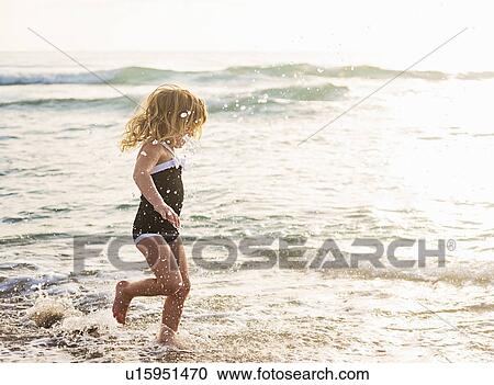 Stock Image - Girl (4-5) running in water on beach. Fotosearch