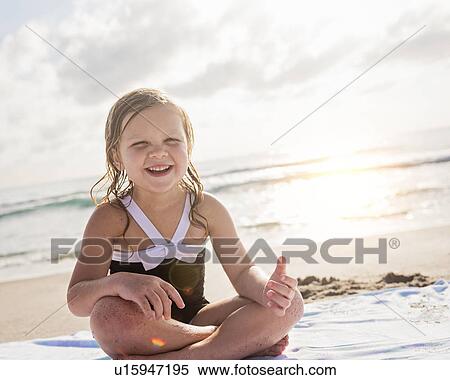 Stock Photography - Girl (4-5) sitting cross- legged on beach. Fotosearch