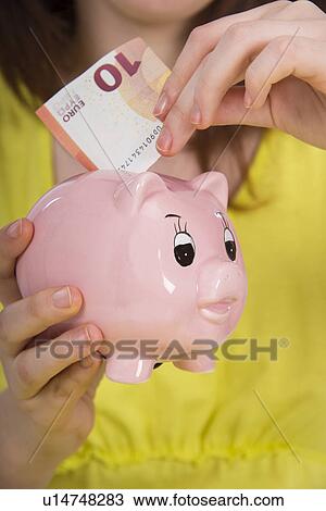 Stock Image - Girl saving euros in piggy bank. Fotosearch