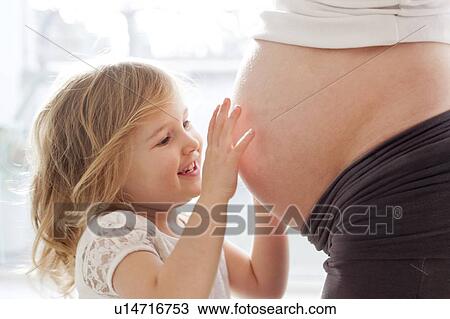 Stock Image - Girl touching pregnant mother's tummy. Fotosearch