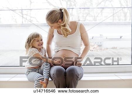 Stock Photograph - Girl touching pregnant mother's tummy. Fotosearch