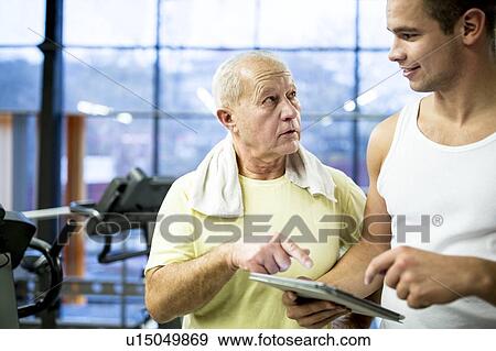 Stock Photo - Gym trainer showing tablet to senior man. Fotosearch