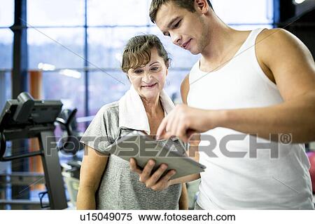 Gym trainer showing tablet to woman View Large Photo Image Stock Photography - Gym trainer showing tablet to woman. Fotosearch