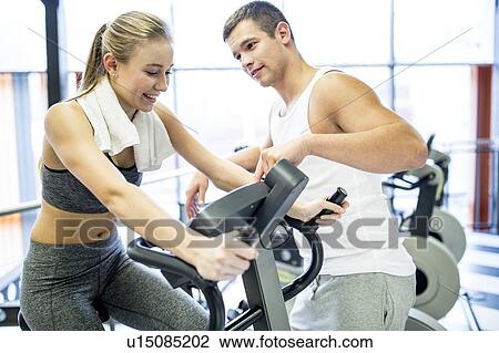 Stock Image - Man instructing woman in gym. Fotosearch