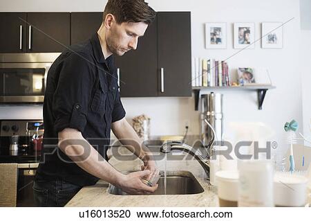 Stock Image - Man washing drinking glass in kitchen. Fotosearch