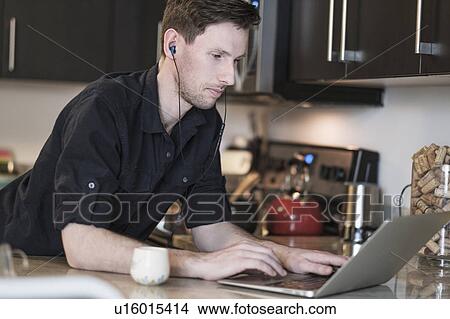 Picture - Man working on laptop computer in kitchen. Fotosearch