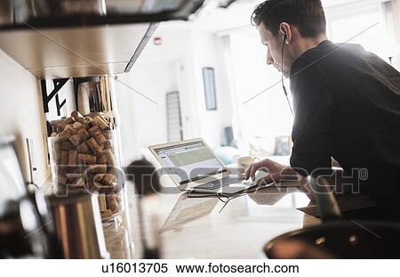 Stock Photography - Man working on laptop computer in kitchen. Fotosearch