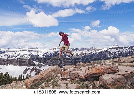 Stock Photo - Mid adult man jumping over rocks in mountains. Fotosearch