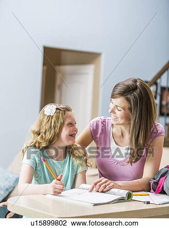 Stock Image - Mother and daughter (8-9) sitting at table doing homework. Fotosearch