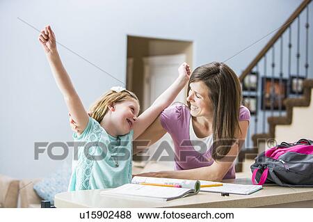 Stock Photo - Mother and daughter (8-9) sitting at table doing homework. Fotosearch