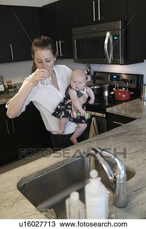 Mother drinking water while holding baby daughter (2-5 months) View Large Photo Image Stock Image - Mother drinking water while holding baby daughter (2-5 months). Fotosearch