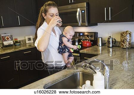 Mother drinking water while holding baby daughter (2-5 months) View Large Photo Image Stock Photo - Mother drinking water while holding baby daughter (2-5 months). Fotosearch