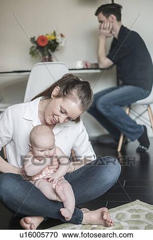 Mother holding baby (2-5 months) and father working in background View Large Photo Image Stock Image - Mother holding baby (2-5 months) and father working in background. Fotosearch