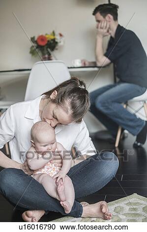 Mother holding baby (2-5 months) and father working in background View Large Photo Image Stock Image - Mother holding baby (2-5 months) and father working in background. Fotosearch