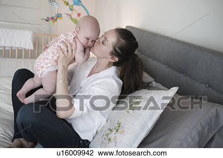 Stock Image - Mother kissing baby daughter (2-5 months) in bedroom. Fotosearch