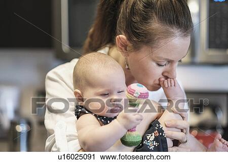 Stock Image - Mother kissing baby daughter's (2-5 months) feet. Fotosearch